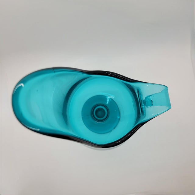Mid-century modern glass pitcher in a vibrant turquoise blue, featuring a striking asymmetrical silhouette and an elegant...
