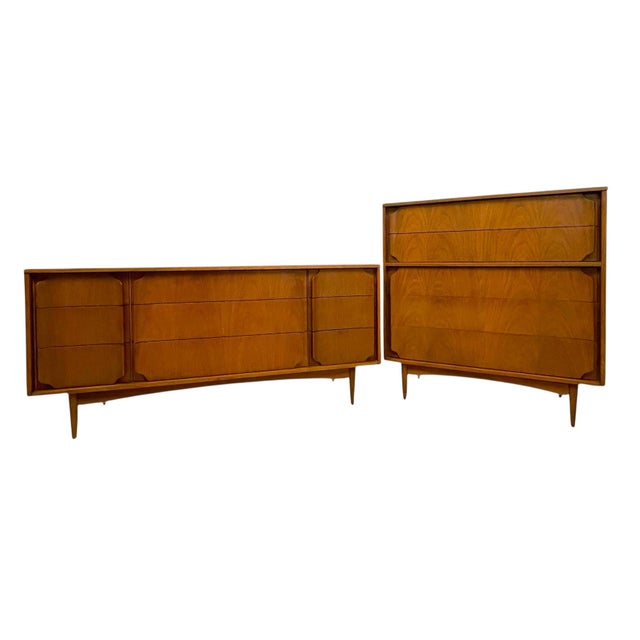 A coordinated two-piece Mid-Century Modern dresser set featuring sculpted drawer fronts, warm wood tones, and clean,...