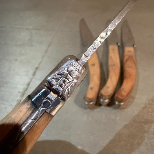 For your consideration, a set of Laguiole-style steak knives featuring their characteristic curved wooden handles,...