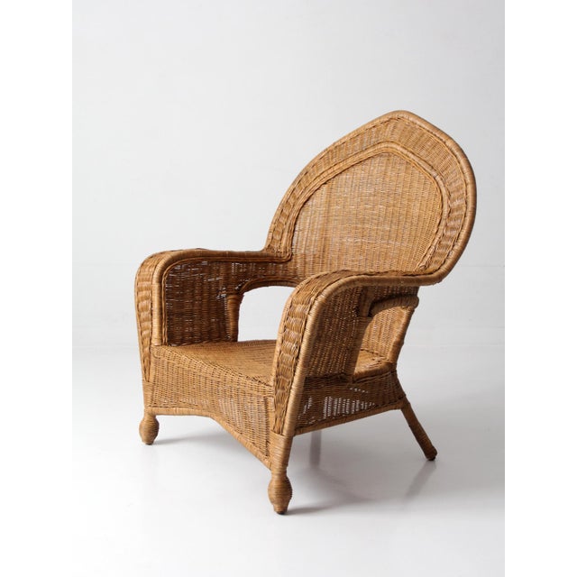 A vintage wicker armchair with a high, shaped back and gently curved arms, finished in a warm honey tone that lends an...