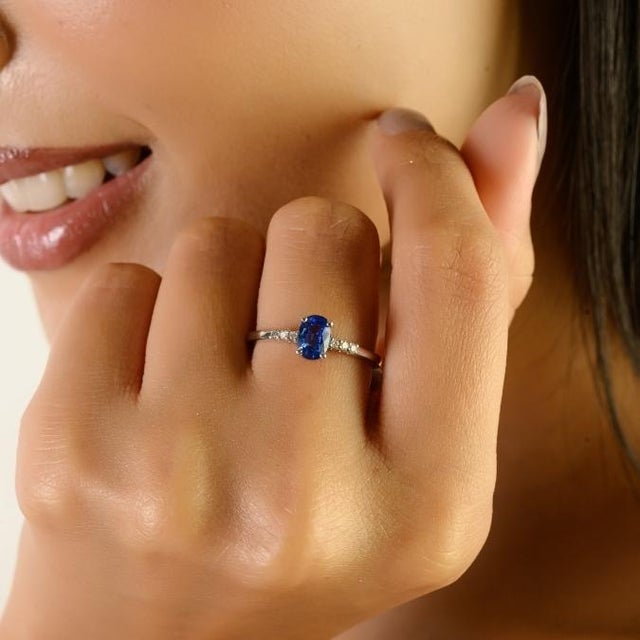 This elegant solitaire ring features a captivating oval-cut natural blue sapphire weighing approximately 0.76 carat,...