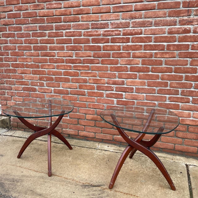 A sculptural pair of side tables designed by Forest Wilson, each featuring a curved walnut base supporting a round glass...