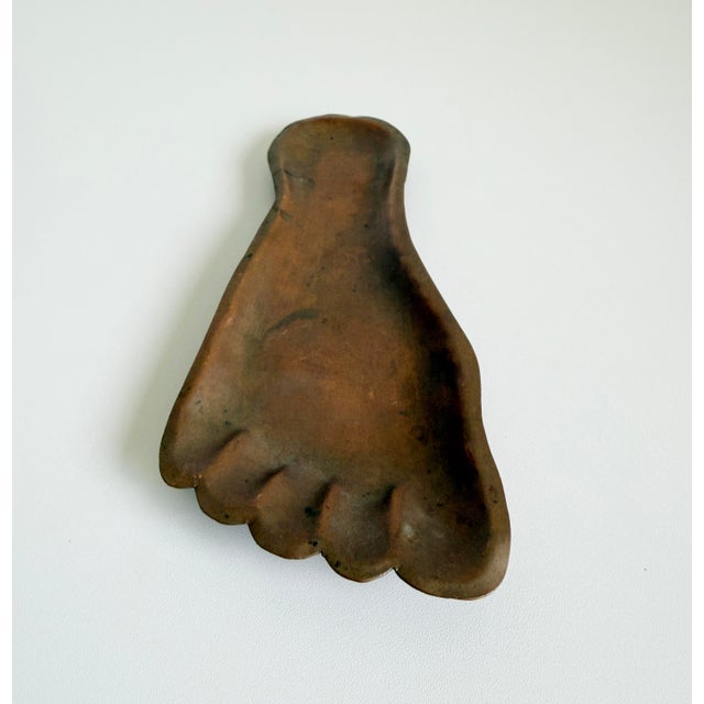 A vintage, circa 1960s, copper metal foot catchall or ashtray. It features a stylized, anatomical human foot shape with...
