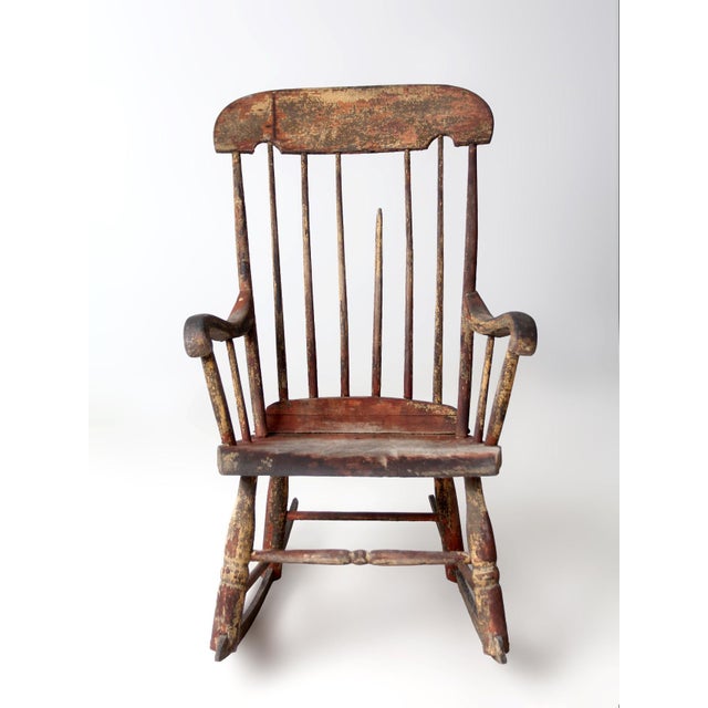 A late 19th century American rocking chair influenced by Windsor and folk traditions, featuring a tall spindled back,...