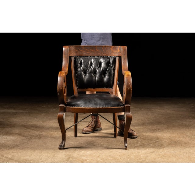 Antique leather and oak chair with tufted upholstery. This piece features a carved oak frame with scrolled armrests. The...