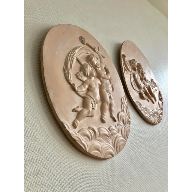 Pair of large medallions with putti in low relief from the 20th century, representing 2 loves or putti in the clouds....