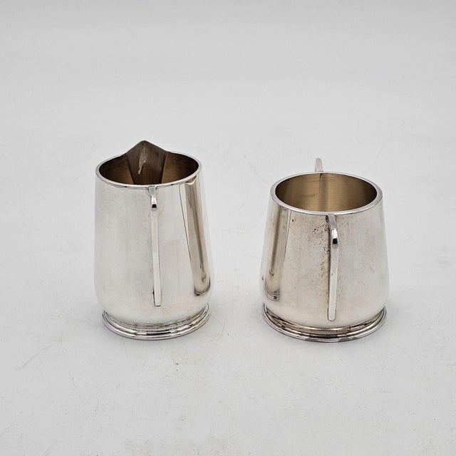 A sterling silver cream and sugar, U.S.A. circa 1930. The creamer measures 3" h x 3.5" w x 2.5" d, and the sugar bowl...