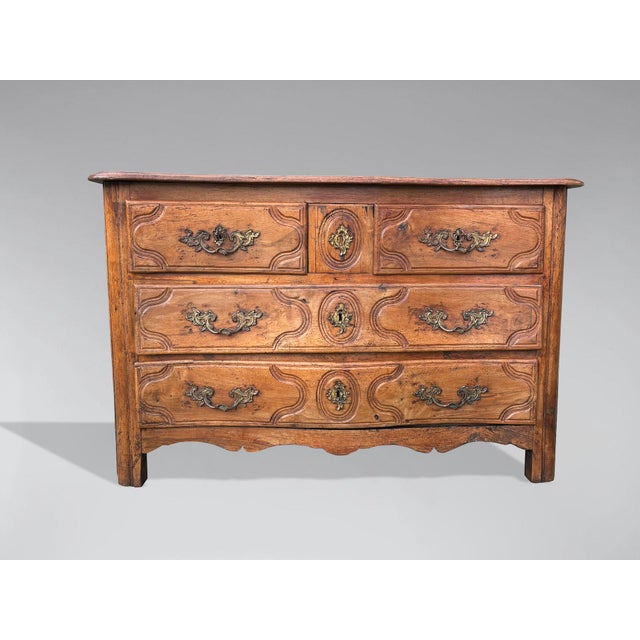 A mid-18th-century walnut French provincial commode from the Louis XV period. This chest of drawers features three levels,...