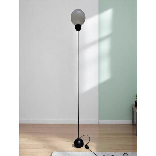 Floor lamp from the 1970s characterized by a slender, vertical stem rising from a circular base.The stem is made of black...