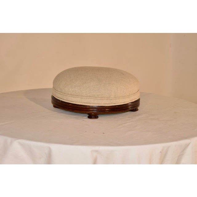 Early 19th century turned mahogany footstool from England. The top has been newly upholstered in linen with banded welt...