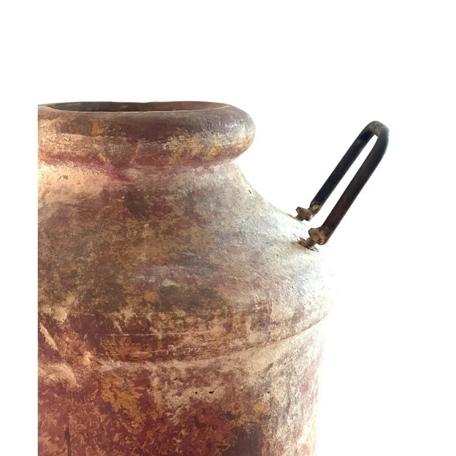 Heavy terracotta vase with warm reddish-brown hue that exudes a rustic charm, while the metal handles introduce a...