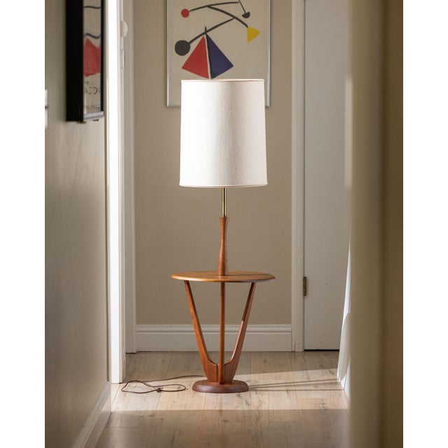 A sculptural mid-century modern floor lamp in walnut featuring an integrated circular side table and solid brass column....