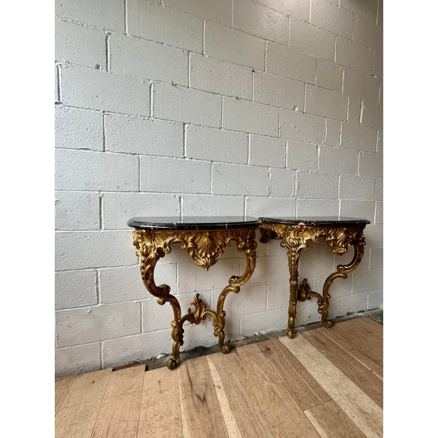 A striking pair of Rococo Revival wall consoles featuring richly carved scrolling acanthus foliage, shell motifs, and...