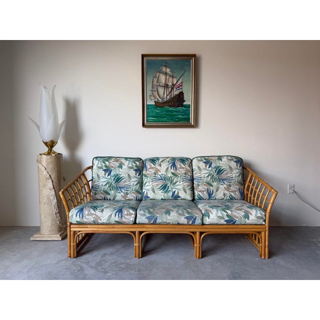 This vintage bamboo and rattan sofa, designed in the style of Ficks Reed, features a classic coastal and tropical...