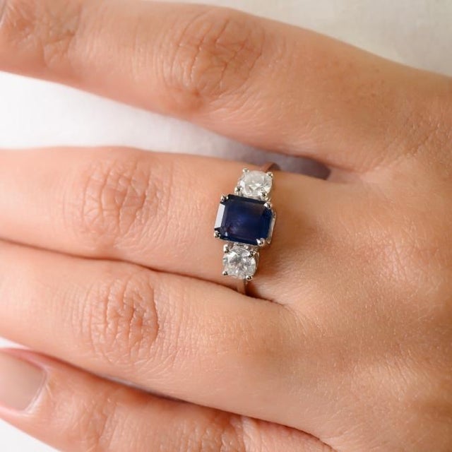 This elegant three-stone engagement ring features a one natural blue sapphire totaling 0.97 carats, set in rich 14k white...