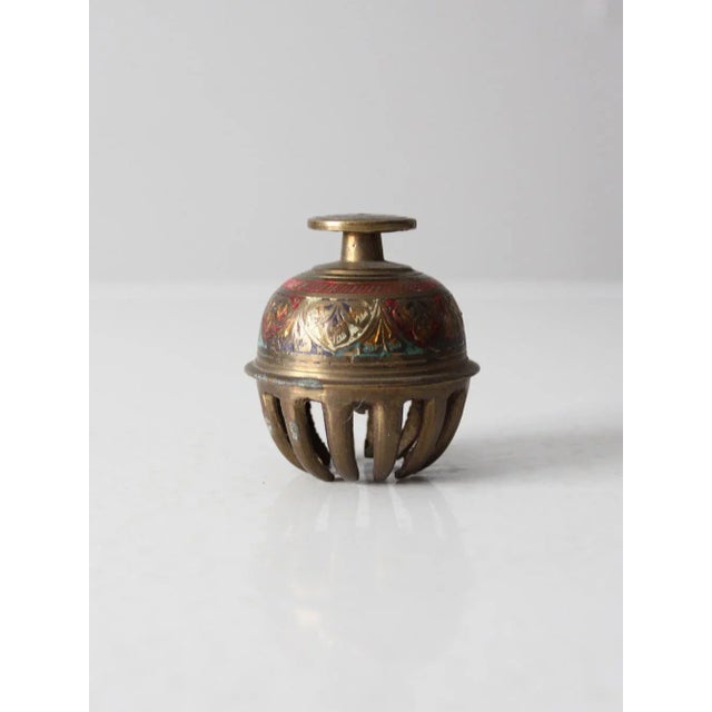 This is an antique Indian elephant claw bell. The brass bell has a lovely etched pattern with enamel painted accents.