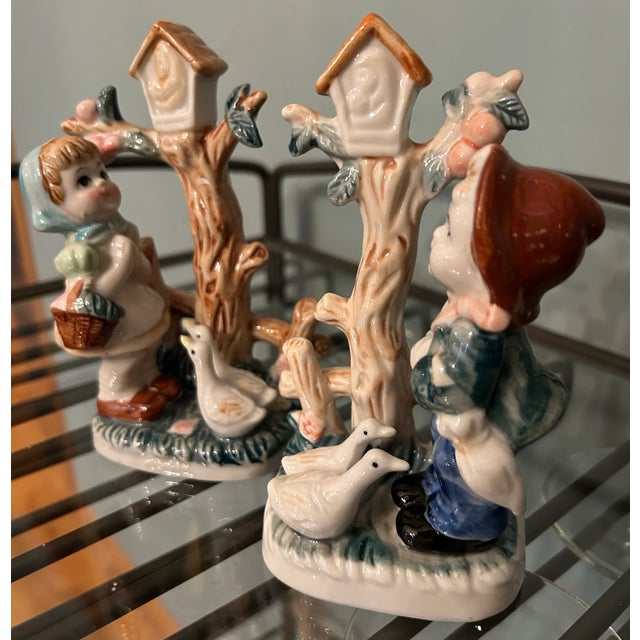 Lot of Two Vintage Hummel-Like Style Porcelain Figurines of Boy and Girl with trees and birdhouses features hand-painted...