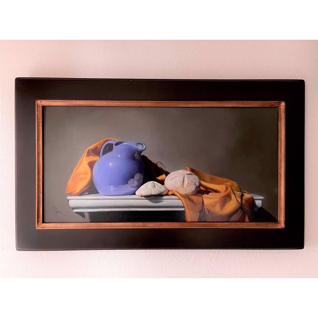 This artwork features a serene still life composition, showcasing a vibrant blue jug, a pair of sand dollars, and a warm...