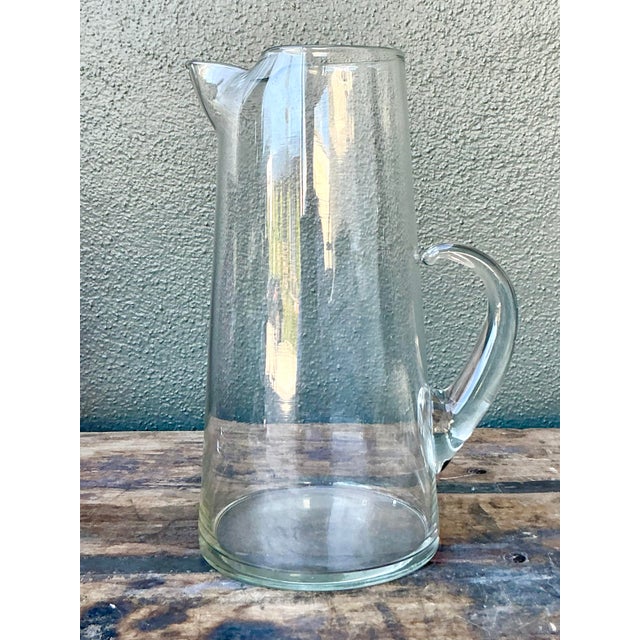 Embrace the elegance of pure form with this striking vintage hand-blown glass pitcher. Characterized by its tall,...