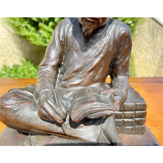 Bronze with brown patina Meiji period representing a scholar sitting writing. The subject is presented on a small square-...