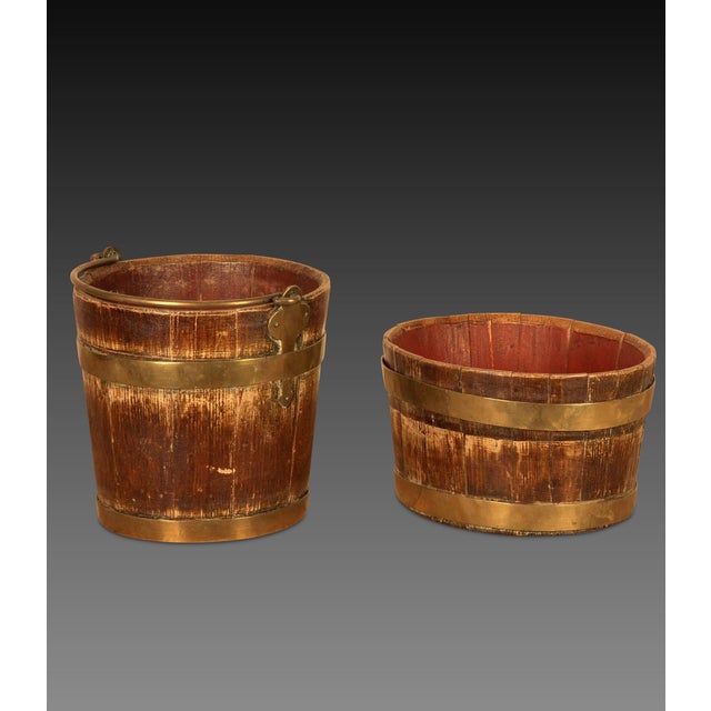 A duo of early C19th coopered buckets, of tapering form, one circular, one oval, both finished in the original grained...