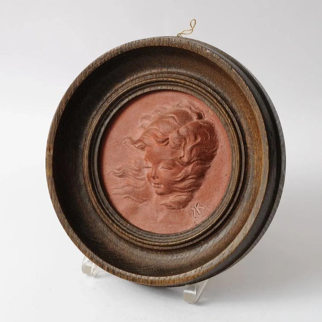 Terracotta relief of a young girl in a round wooden frame. Made by Koos van der Kaaij (1899-1976). Signed with artist...