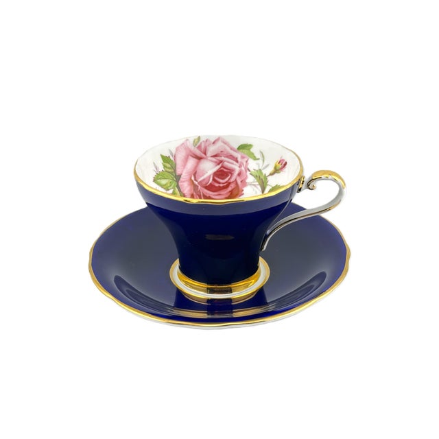 A striking cobalt blue Aynsley bone china corset-shaped teacup and saucer, decorated inside the cup with a large pink...