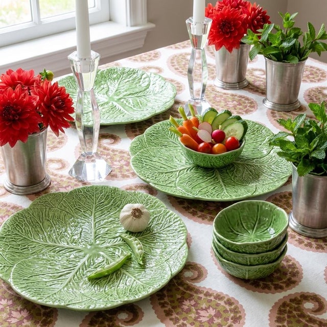 A cabbage leaf platter carries a smaller dip bowl nested among hand-painted peas and a garlic bulb, a classic majolica...