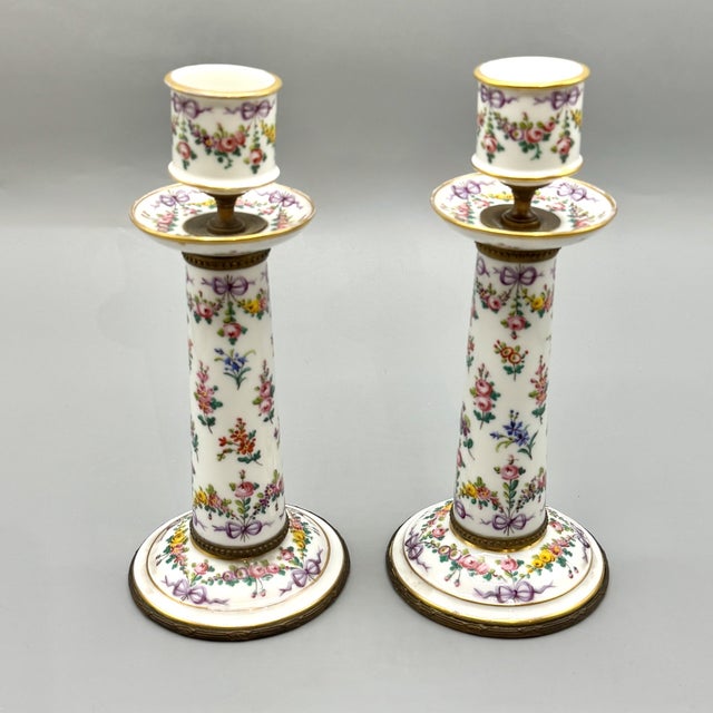 An elegant pair of sèvres-style porcelain candlesticks, beautifully hand-painted with delicate floral garlands and...