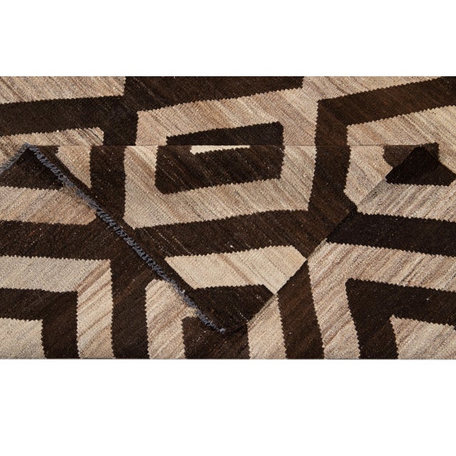 Beautiful hand-knotted wool, modern Turkish Kilim wool rug. This rug features a brownfield with abstract, tan interlocking...