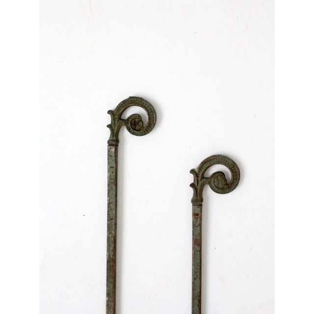 A pair of antique drapery hangers featuring metal slide-out poles დასრულated with decorative curled foliage finials. The...