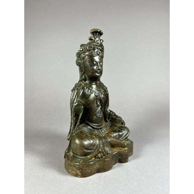 The Bronze Bodhisattva is seated upright in a lotus position or padmasana, a meditation pose on a base. The hands are in a...