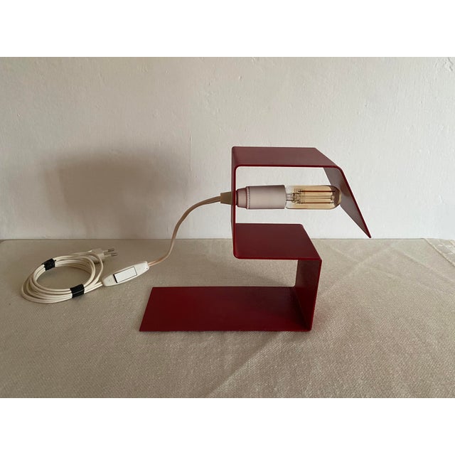 A striking vintage table lamp dating from the 1970s, featuring a bold geometric form and a vibrant red finish. Its...