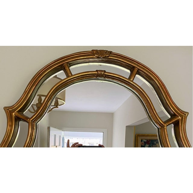 A vintage large arched framed rectangular gilded wall mirror by Carolina Mirror with a warm, gold tone finish, scalloped-...