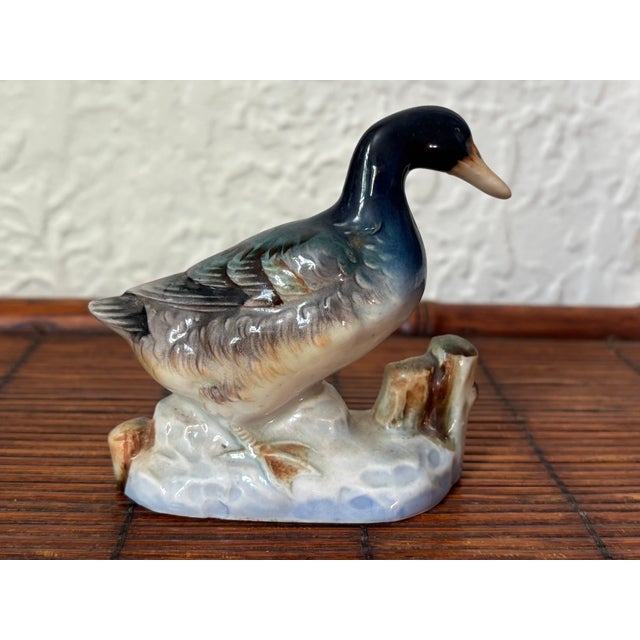 Glazed in blue, this porcelain duck figurine stands on the shoreline. The beak and feet are glazed in pale yellow and the...