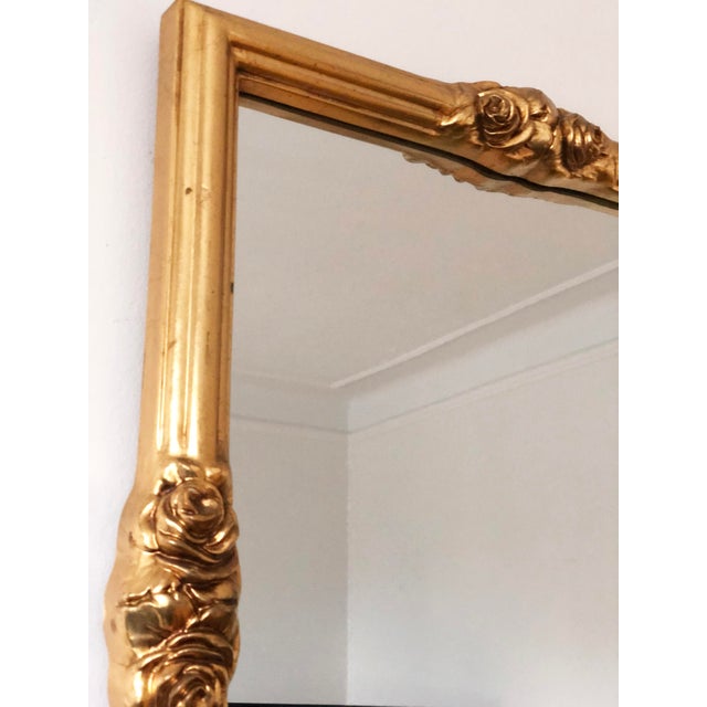 A giltwood beveled mirror with golden rose accents, inspired by Rococo style and made in Italy around 1960. Object: Mirror...