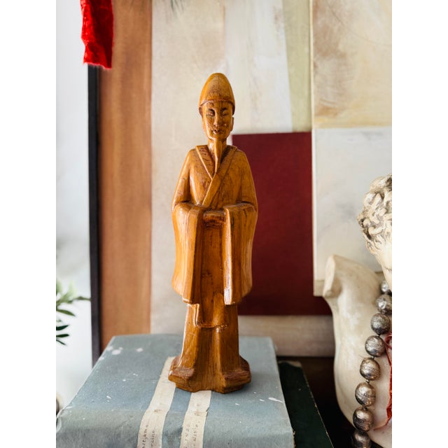 A beautifully hand-carved wooden figure depicting a robed scholar or elder, rendered with a calm expression and graceful...