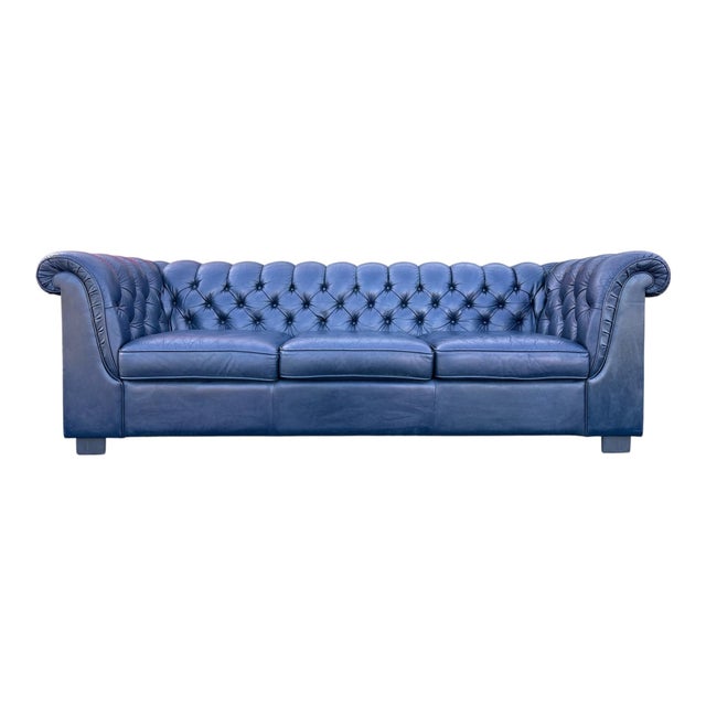 A three-seater sofa in blue leather in the Chesterfield style, with deep button-tufting across the back, rolled arms and...