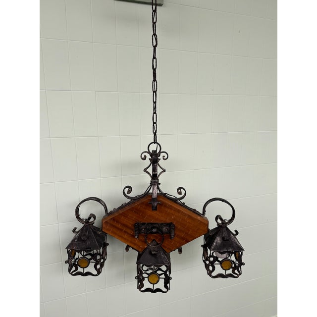This decorative chandelier combines wrought iron, glass, and crafted wood in a composition with a strong artisanal feel....