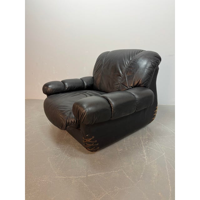 Striking black leather lounge chair with distinctive lace detailing at the corners and brass buttons on the back....