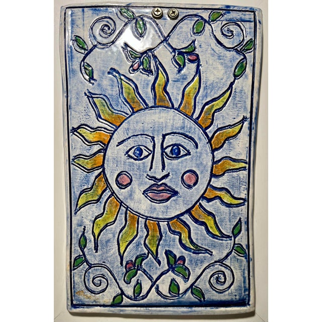 Vintage handmade ceramic wall plaque featuring a stylized sun design, beautifully mounted on a wooden base. The plaque has...