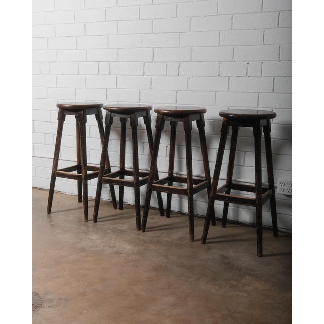 This set of four vintage wooden bar stools exudes rustic charm with their weathered dark finish and sturdy, classic...