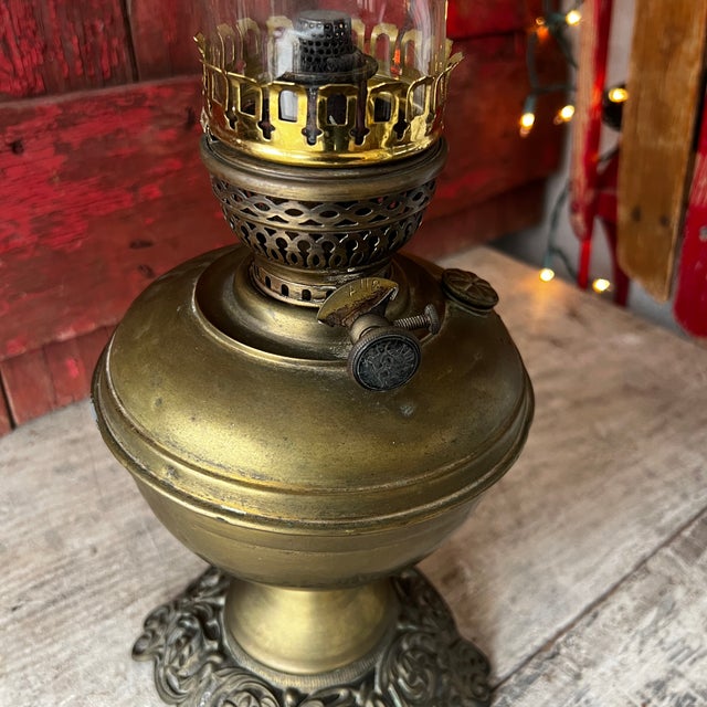 This antique brass oil lamp features intricate Victorian designs on its ornate base and a clear glass chimney. A...