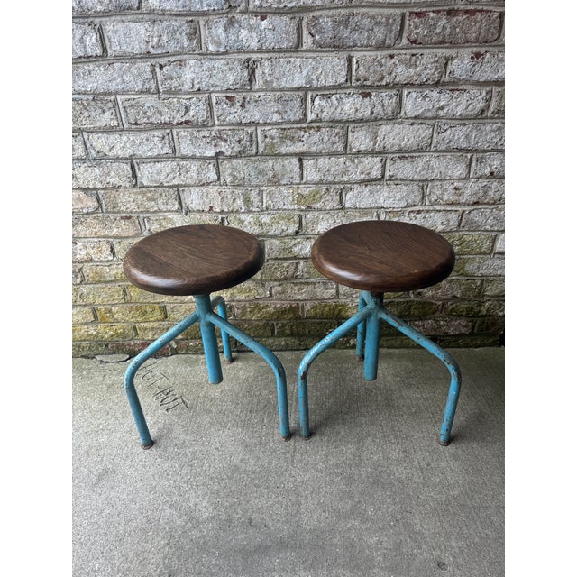 Pair of vintage artists stools on blue metal bases with round dark wood tops. These industrial metal stools have an...