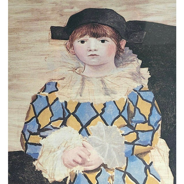 This framed print is a 1980 limited-edition offset lithograph after Pablo Picasso's famous 1924 painting Paul en Arlequin...
