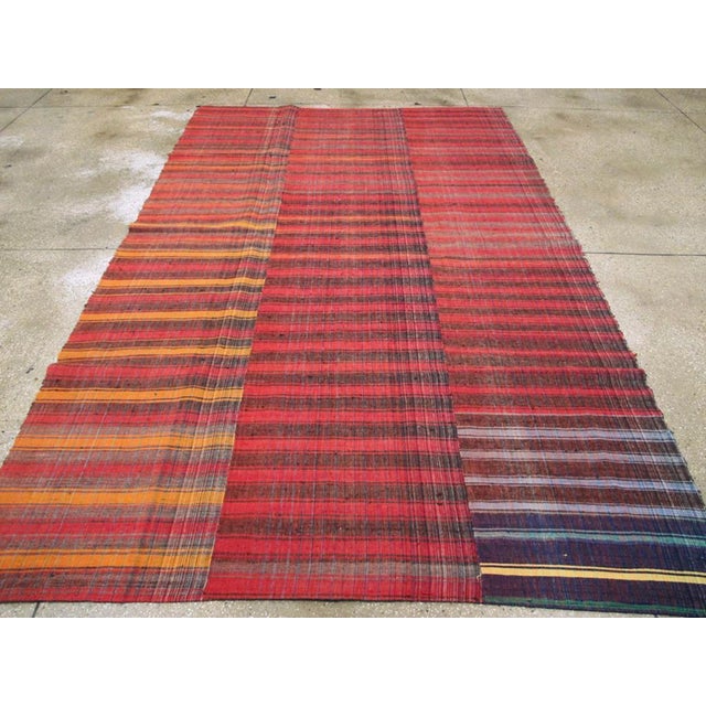 This mid-20th century Turkish flatweave kilim rug, features a vibrant composition of horizontal stripes woven across three...