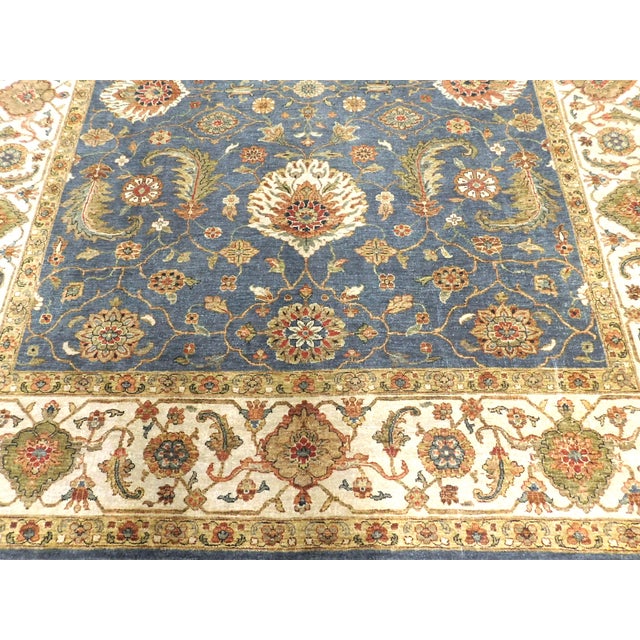 Handmade wool rug featuring an ornate floral and botanical palmette motif with a blue field and contrasting ivory border....