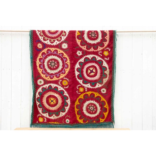 This colorful vintage Suzani tapestry hails directly from Uzbekistan. The background boasts a luxurious brick red hue, a...