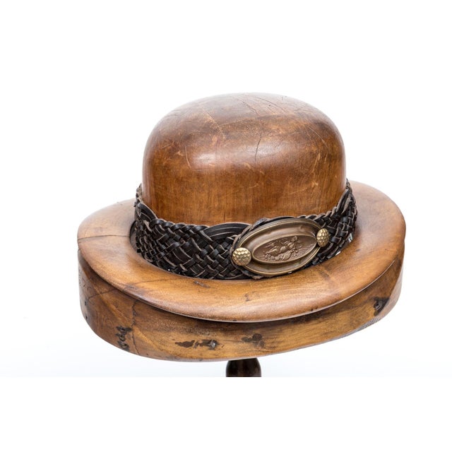 A carved wooden hat block shaped like a bowler hat with a weathered wood grain and scattered workshop nail holes, domed...