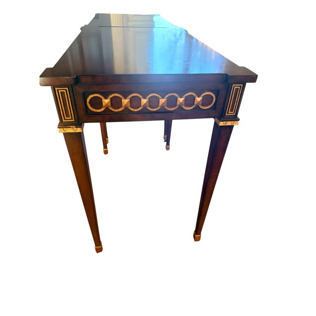 This table's design, featuring a dark wood finish, gold inlay in a chain-link motif, and tapered legs, suggests a piece...